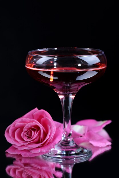 Composition with pink sparkle wine in glass and  rose isolated on black