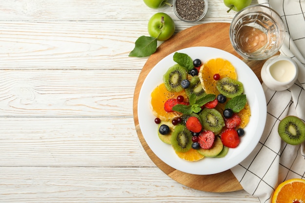 Composizione con piatto di insalata di frutta fresca sulla tavola di legno bianca