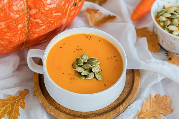 Composition with pot of tasty pumpkin cream soup and autumn leaves on wooden background