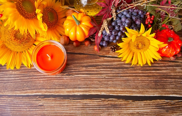 カボチャ、秋の紅葉、ブドウ、ヒマワリ、キャンドル、木製のテーブルの上の果実のコンポジション
