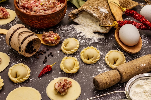 Composition with raw dumplings and ingredients on trendy black stone concrete background. Process of cooking