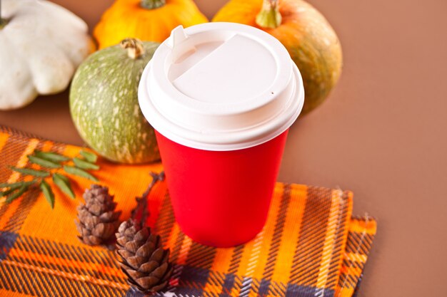 Composition with red paper cup with tea, autumn leaves and small pumpkins on the brawn background. Autumn harvest. Autumn concept.