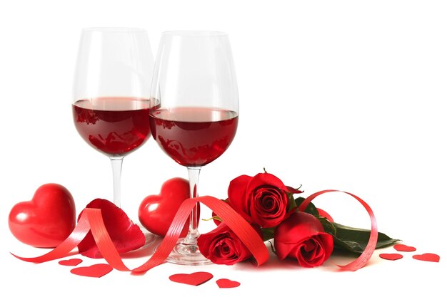 Composizione con vino rosso in bicchieri, rose rosse, nastro e cuori decorativi su sfondo chiaro