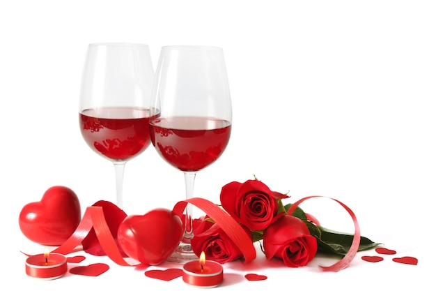 Composizione con vino rosso in bicchieri, rose rosse, nastro e cuori decorativi su sfondo chiaro