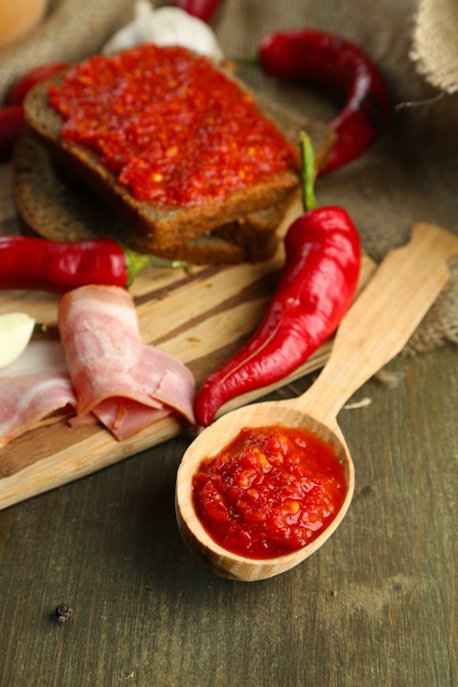 Composition with salsa sauce on bread, red hot chili peppers  and garlic, on sackcloth,  on wooden wall