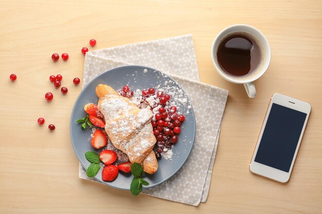 木製の背景においしいクロワッサン コーヒーと携帯電話のコンポジション