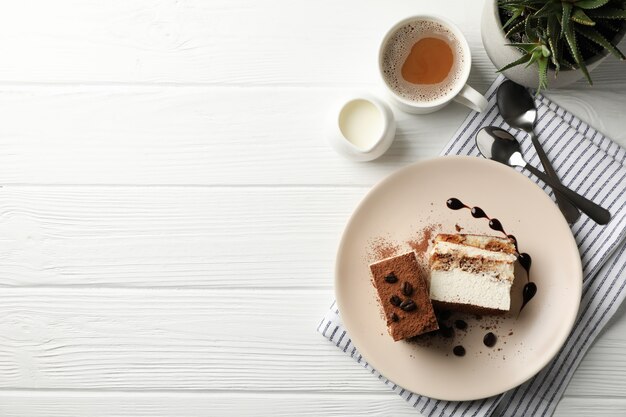 Composition with tasty tiramisu and cocoa drink on white wooden table.