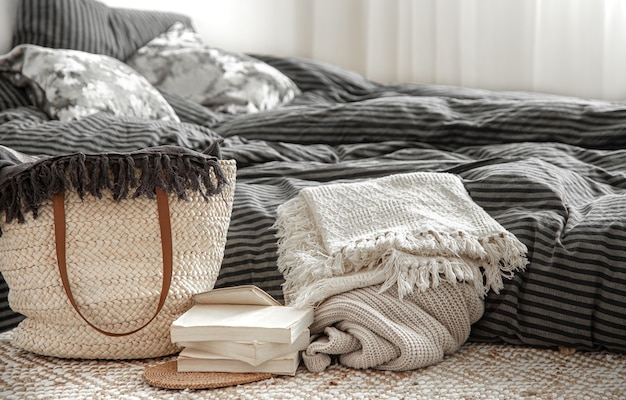 Photo composition with wicker straw large bag, blankets and books in a bedroom.