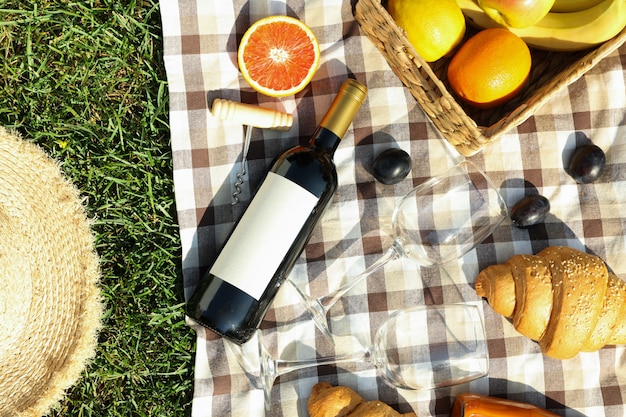 Composition with wine, croissants, fruits and towel on grass