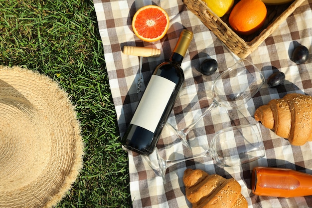 Composition with wine, croissants, fruits and towel on grass