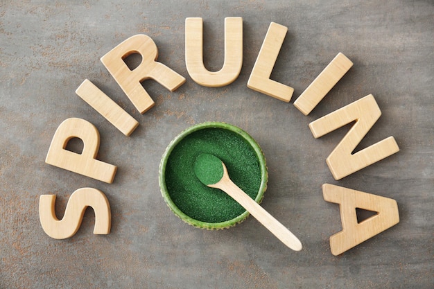 Composition with wooden letters and bowl with spirulina powder on table