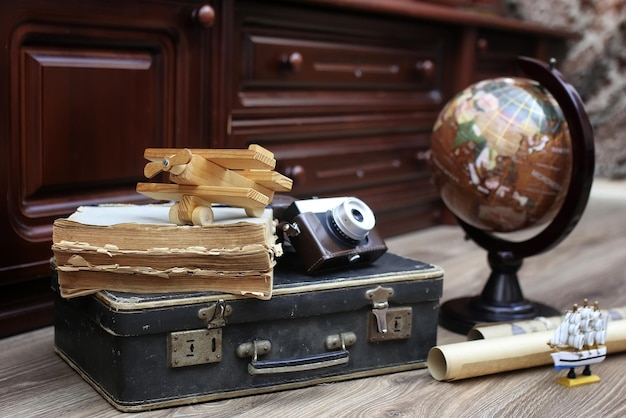 Composition on a wooden floor vintage globe with old leather suitcase with objects for travel