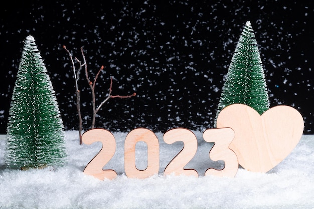 Photo a composition of wooden numbers of the year 2023 and a heart in a snowcovered forest during a snowfall at night