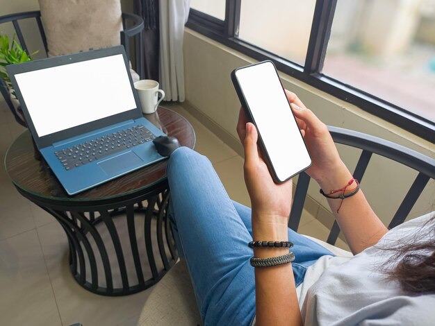 Computer blank screen phone mockup image with white background\
for advertising woman39s hand using laptop and mobile phone on\
table in cafemockup