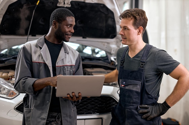 Computer car tuning two smiling auto mechanic testing a car engine connected to laptop in auto repai