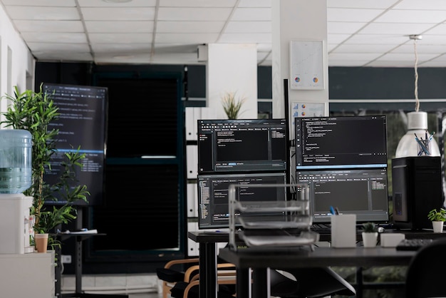 Computer displays on table running programming code html\
algorithms in empty coding agency room. database network servers\
cloud computing in software company, data script language.