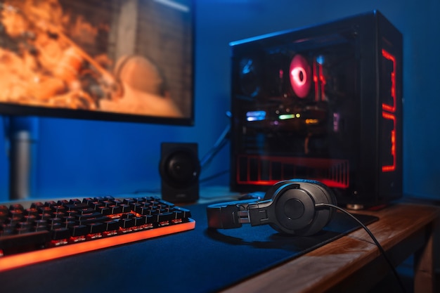 Computer gamer workplace with new game keyboard, mouse, headphones, modern pc with blur blue and red neon light.