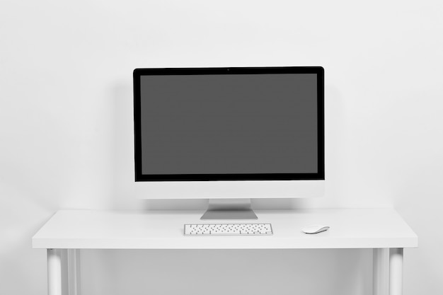 The computer is on a white table on a white , on the table is a keyboard and a computer mouse