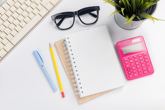 Computer keyboard and note book with pen and pencil on white desk