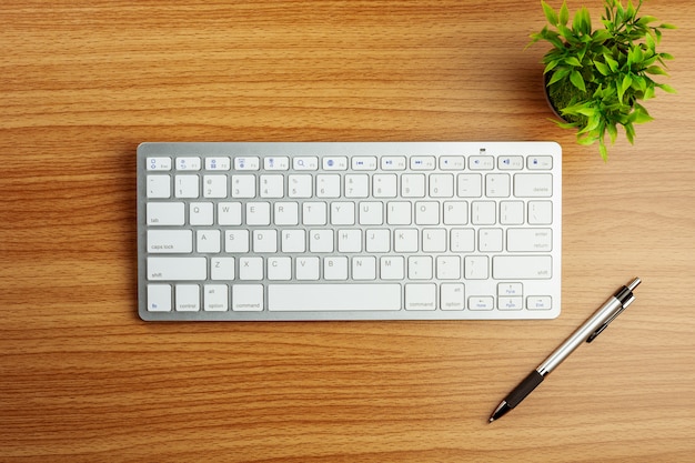 Computer keyboard and a pen on wooden desk background.