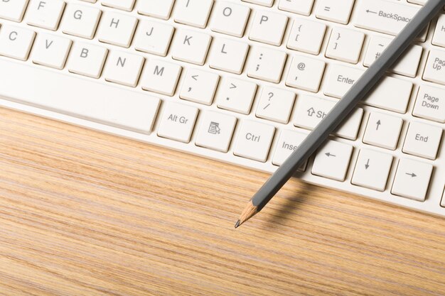 Компьютерная клавиатура и карандаш на столе, вид сверху