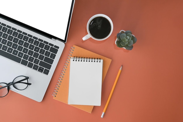 Computer laptop blank notebook cup of coffee and glasses on orange background Flat lay