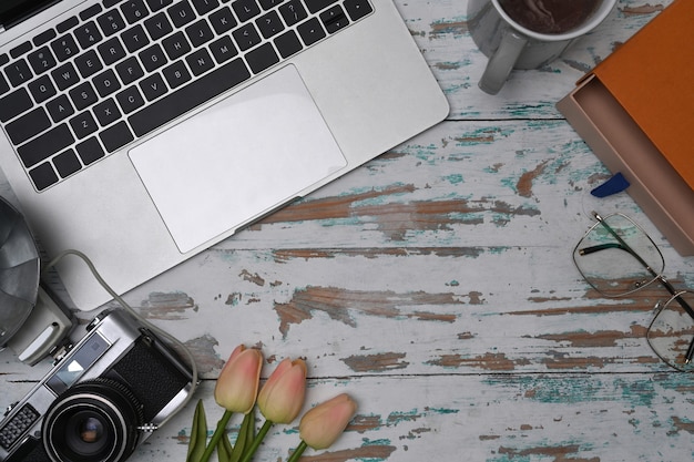 Computer laptop, camera, coffee cup and notebook on wooden table.