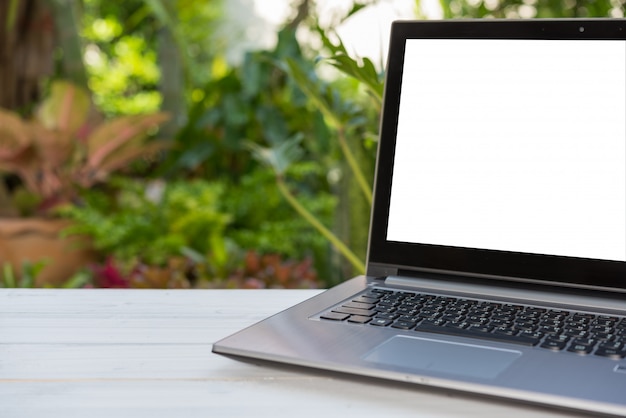 Computer laptop met leeg wit scherm op houten tafel met groene tuin natuur achtergrond