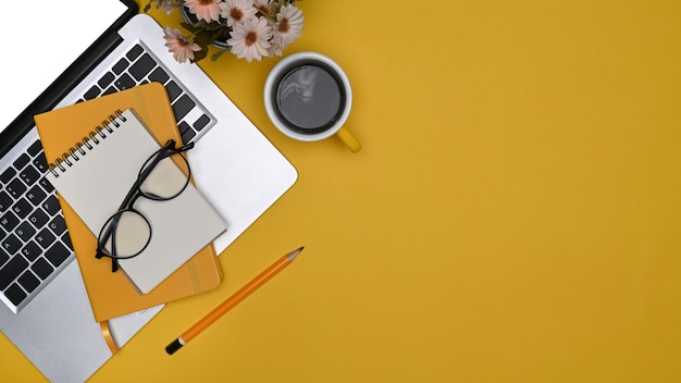 Computer laptop notepad glasses and coffee cup on yellow background