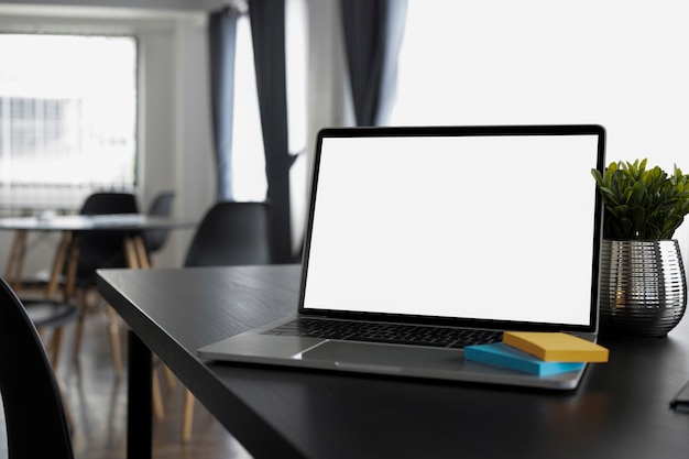 Computer laptop, sticky note and houseplant on black wooden table.