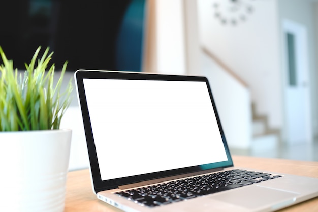 Computer portatile con lo schermo in bianco sulla tavola del fondo della sfuocatura della stanza vivente con bokeh, monitor in bianco del modello dell'ufficio del lavoro dello scrittorio