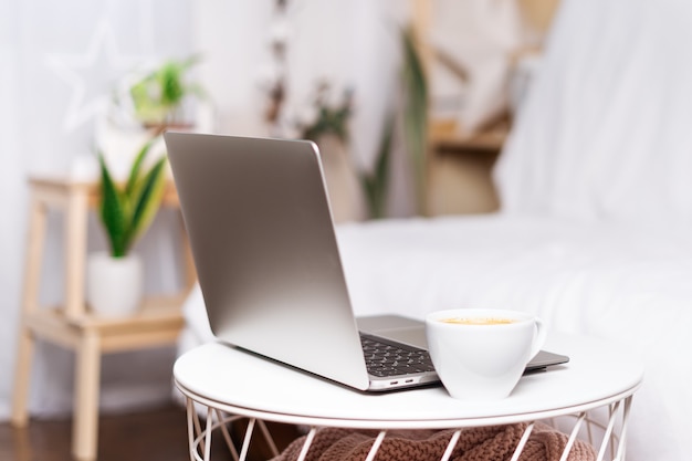 Computer laptop with coffee in white cup at home background. Work remotely or from home. Selected focus. Copy space.