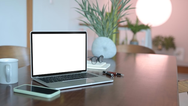 Ноутбук с белым экраном, смартфон и очки на деревянном офисном столе