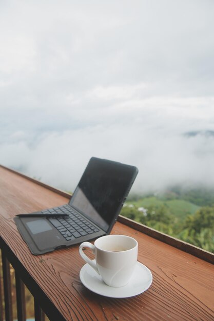 Computer Monitor Keyboard coffee cup and Mouse with Blank is on the work table at the sky mountain river and trees front view background