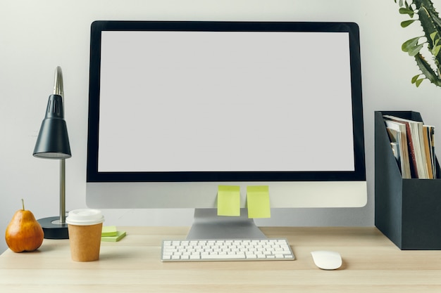 Photo computer monitor with mockup white screen on office table with supplies