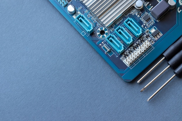 Computer motherboard and three small screwdrivers on a gray paper