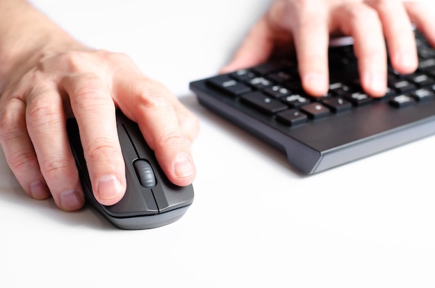 A computer mouse in a man's hand and a black keyboard White background