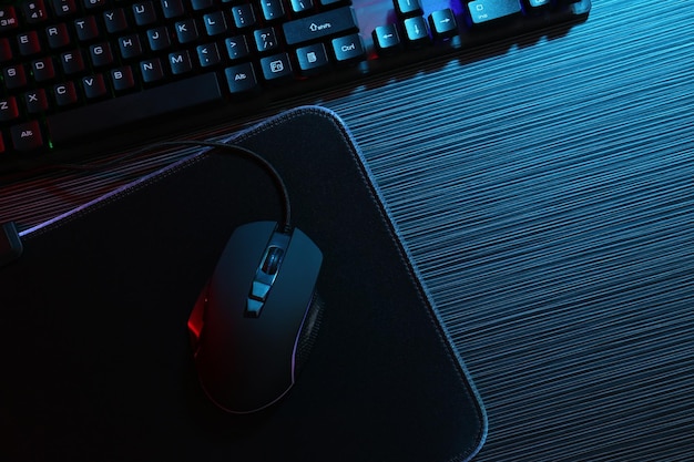 Computer mouse mousepad and keyboard on dark wooden table in neon lights flat lay Space for text
