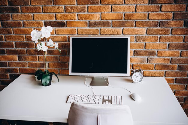 Un computer un taccuino un'orchidea bianca su un tavolo bianco e un muro di mattoni elegante itnreyer casa fuori