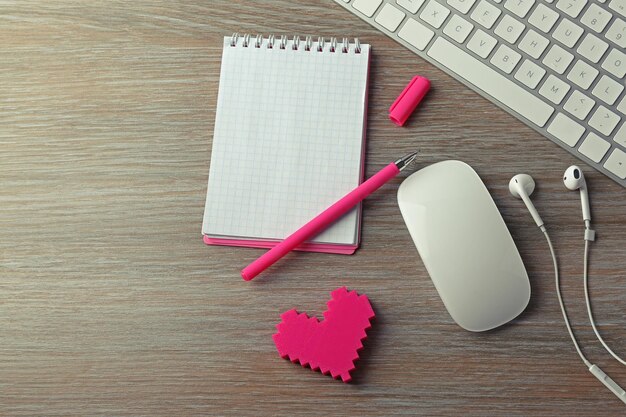 Photo computer peripherals with pink heart pen and notebook on wooden table