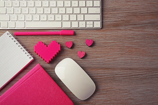 Computer peripherals with pink hearts pen and notebooks on wooden table