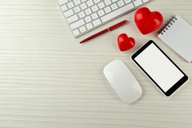 Computer peripherals with red hearts notebook and mobile phone on light wooden table