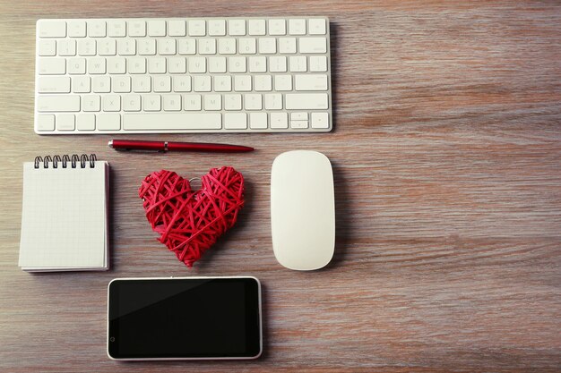 Photo computer peripherals with red wicker heart notebook and mobile phone on wooden table