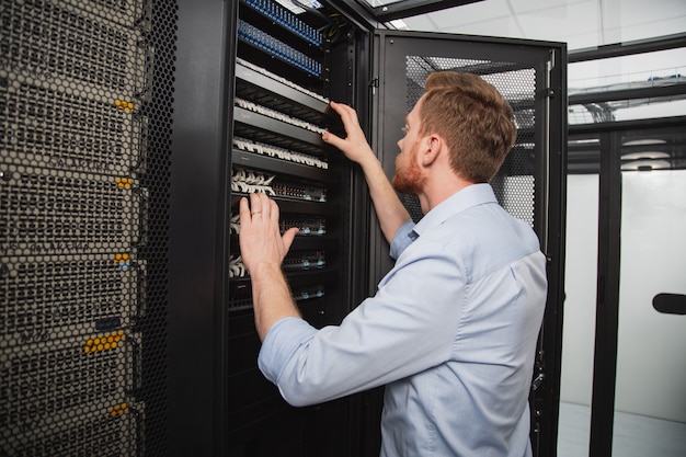 Computer problem. Confident IT technician examining server closet while standing