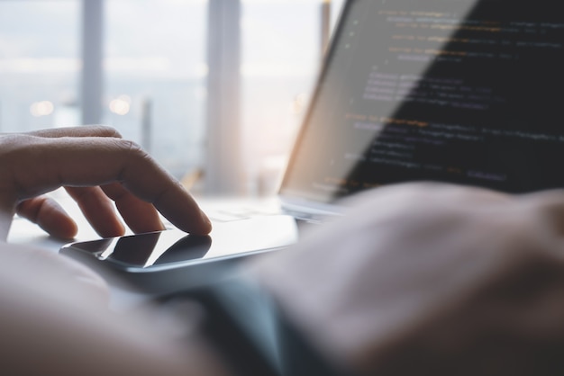 携帯電話を使用し、ラップトップでjavascriptをコーディングするコンピュータープログラマーモバイルアプリ開発者