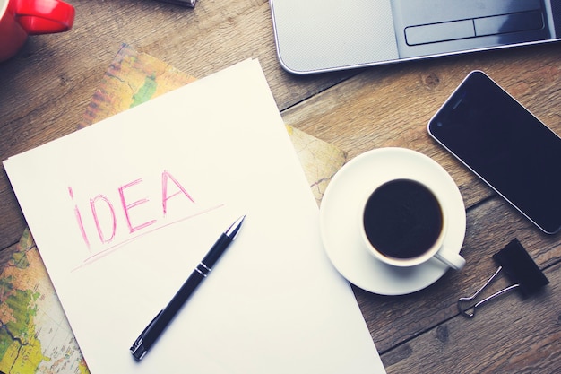 Computer, smart phone, cup of coffee, paper and pen on wooden table