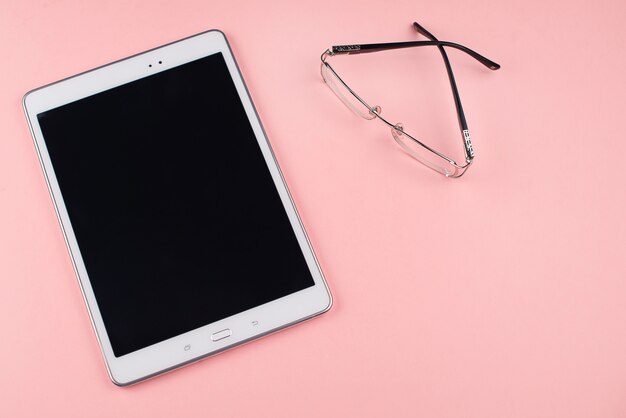 Computer tablet and glasses on a pink background