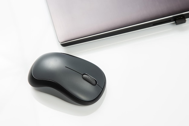 Computer wireless mouse next to a laptop on a white table closeup electronic personal industry