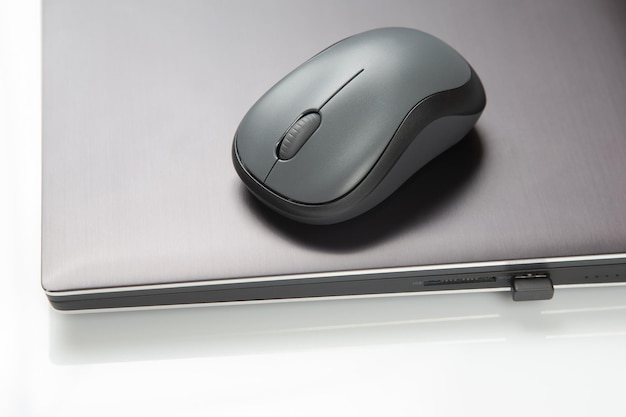 Computer wireless mouse next to a laptop on a white table closeup electronic personal industry