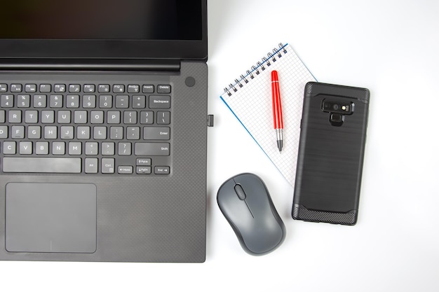 Computer wireless mouse pen and notepad next to a laptop on a white table closeup Items for office work